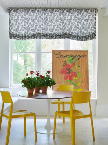 dining table with yellow chairs, floral artwork, and black-and-white curtain