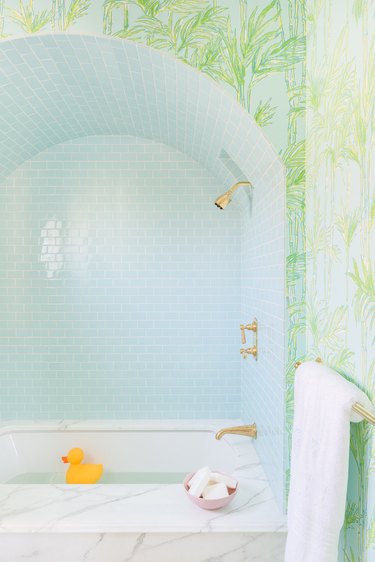 A white marble tub with a light blue backsplash  and bamboo wallpaper.