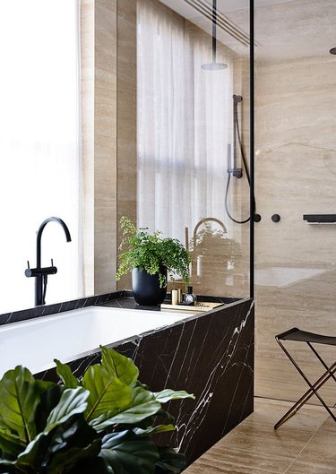 A dark marble bathtub next to neural tiled bathroom.