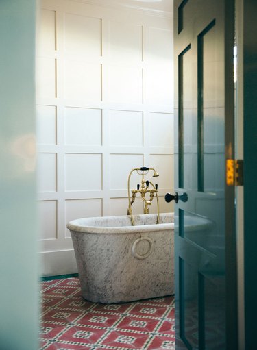 Roman style marble tub on top of red tile flooring.