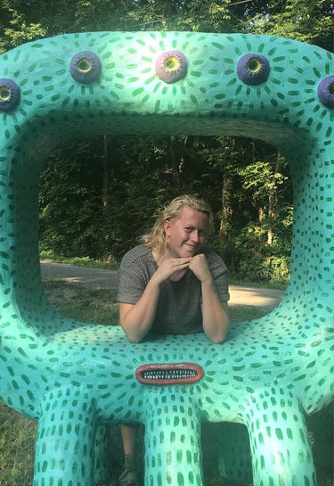 Asher Ford posing in a green art installation with dark green lines all over and purple buttons