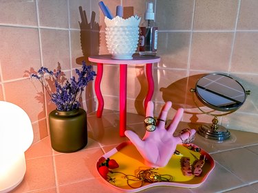 Pink side table, planter, mirror, and pink hand-shaped jewelry holder with low light on tile