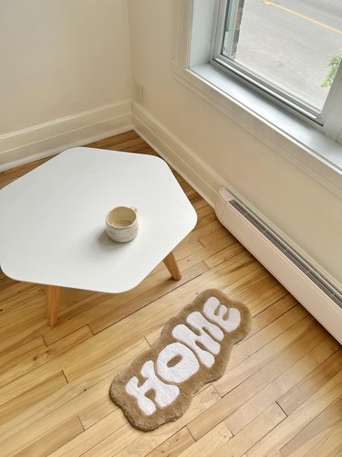 overhead photo of a white table with a mug and a tufted rug that reads "Home"