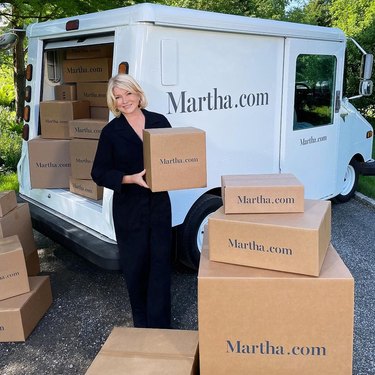 Martha Stewart standing with boxes near a white mail truck that reads "Martha.com"