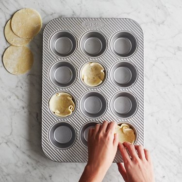 person placing dough into a muffin pan