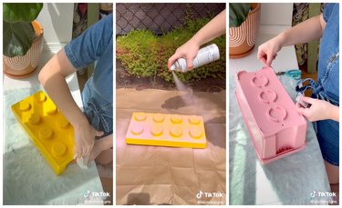 First image is the creator wiping down the giant, yellow LEGO. Second image is the creator spray painting the giant, yellow LEGO pink. The third image is the creator sticking vinyl adhesives to the back of the now pink LEGO box.