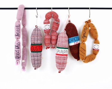 Knitted links of meat hanging on a bar against a white background