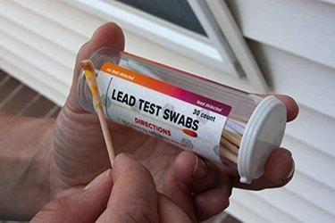 A person holding a lead testing swab outside a house.