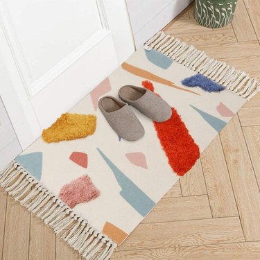 Small fringed area rug with pink, red, blue, and marigold abstract shapes