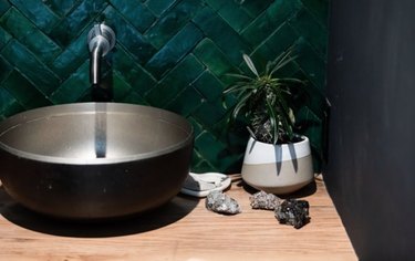 Metal vessel sink with matte green tile backsplash.