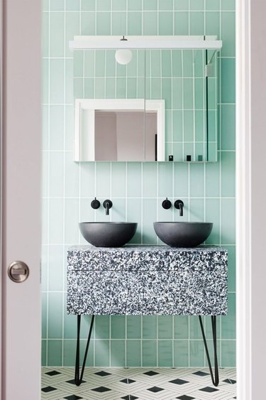 Mid-century modern bathroom with green tile wall, marble vanity, black vessel sinks.