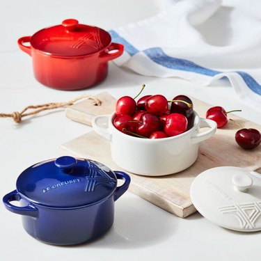 Three small baking dishes. Red and blue ones are closed, white is open and full of cherries
