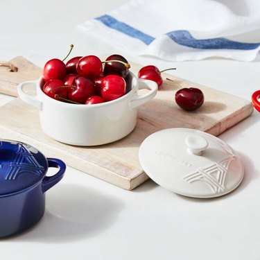 White dish full of cherries on a cutting board