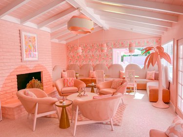 The Trixie Motel pink lobby featuring wavy chandeliers in pink and cream. On the pink armchairs, there are also pillows showing a pink and cream squiggle design.