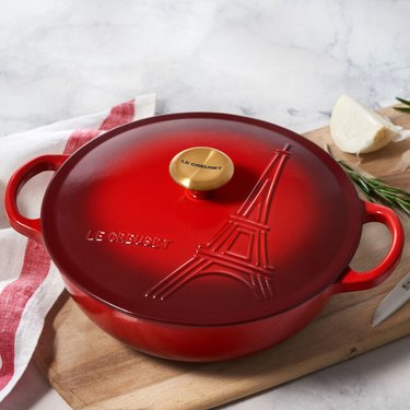 Round, red baking dish with two handles on a cutting board