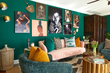 Living room with dark green walls, pink couch with multi-colored pillows, gallery wall with lots of art