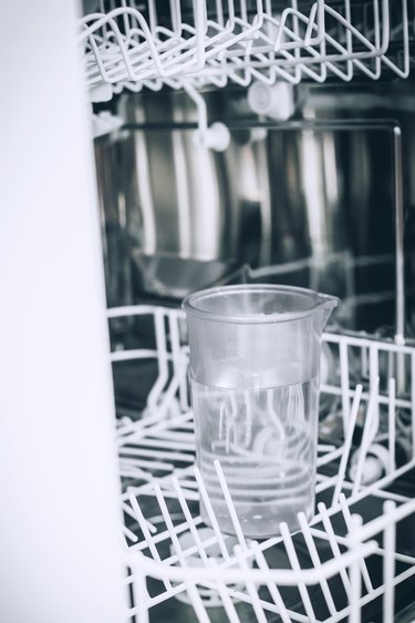 a cup of vinegar on the top rack of a dishwasher