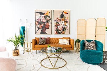 Living room with a rust-colored couch, green chair, brass coffee table, plant, room divider, and paintings on the wall