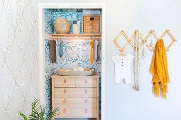 Nursery designed by Jasmine Roth utilizing a closet without doors, hanging pegs, and fun wallpaper