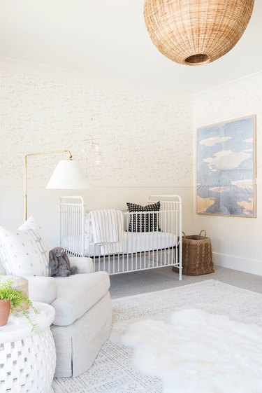 Neutral nursery with cloud painting, cloud rug, rattan lighting, and comfy chair