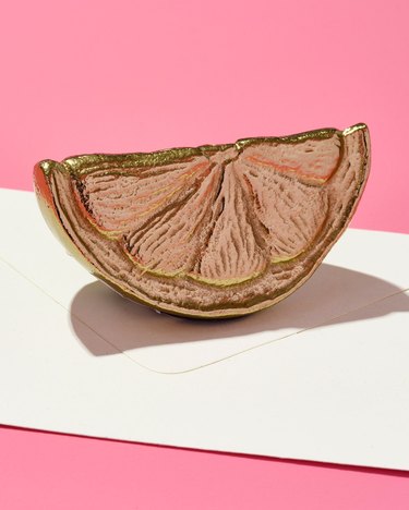 Lemon-shaped gold paperweight on a white and pink background