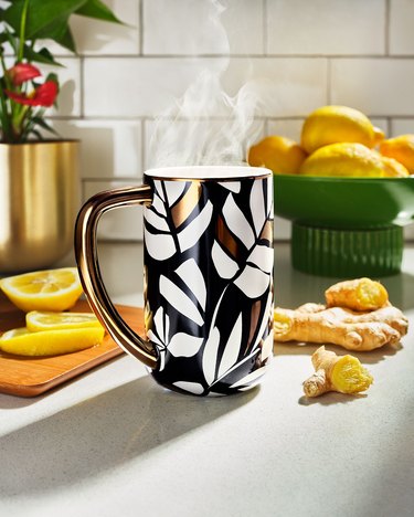 Black mug with a patten of white leaves on a white kitchen counter surrounded by lemons