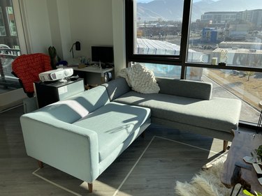 A sectional sofa in a living room apartment. The loveseat side of the sofa is a light blue, while the chaise lounge part of the sofa is gray.