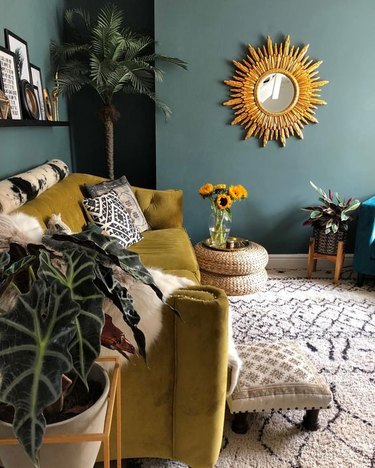 Blue living room with jewel green couch and gold sun mirror.