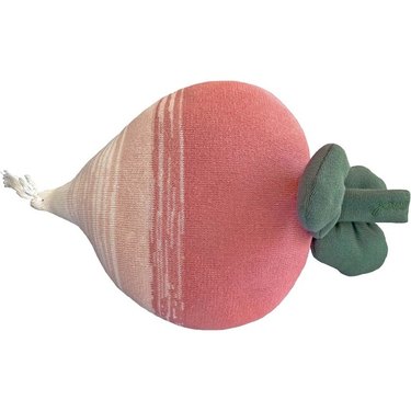 A pink radish pillow that fades to white. On top, there is a green stem and three leaves.