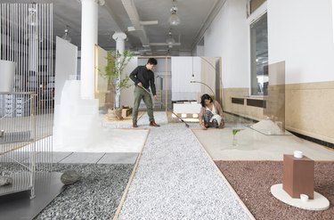 A dark-haired man and woman in a large open white studio space with different colored rocks and materials sectioned off on the floor.