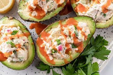 A different angle of the avocados stuffed with chicken salad and drizzled with hot sauce. There is also a sprig of cilantro in the shot.