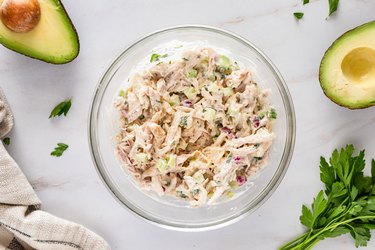 The bowl of mayonnaise, lemon juice, Dijon mustard, salt, ground black pepper, and parsley, but with shredded chicken mixed in.