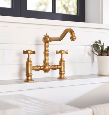 A brass two-handled kitchen faucet in a white kitchen