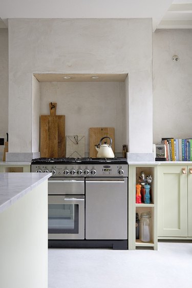 Neutral toned kitchen with soft green lower cabinets and bare plaster walls.