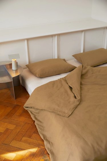 Brown duvet and pillows on white sheets on a mattress on a hardwood floor.