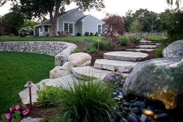 A sloped yard has large boulder stairs that lead down to a grassy path