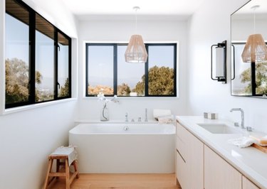 White bathroom with white tub, vanity, wicker pendant.