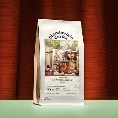 A bag of Chamberlain coffee featuring an illustration of Emma opening her fridge to find a bag of Chamberlain Coffee, strawberries, and little animals like a sheep, a bird, a salamander, and a cat.