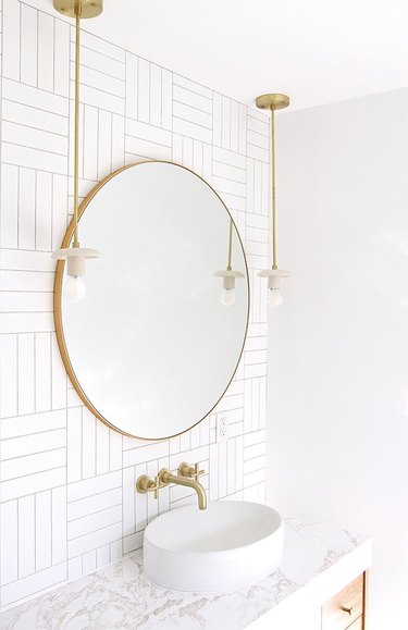 Bathroom vanity with round mirror, subway tile, brass pendants with exposed bulbs, vessel sink, wall-mounted faucet..