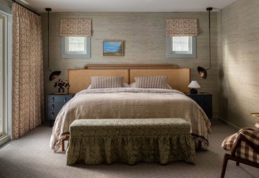 Bedroom with taupe bedding, walls, bench, curtains.