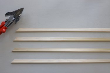 Four unfinished wood molding pieces cut with mitered corners next to miter shears