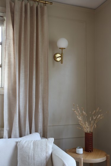 a globe sconce hangs on a taupe wall with wall moldings