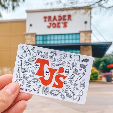 Hand holding a Trader Joe's membership card in front of a storefront
