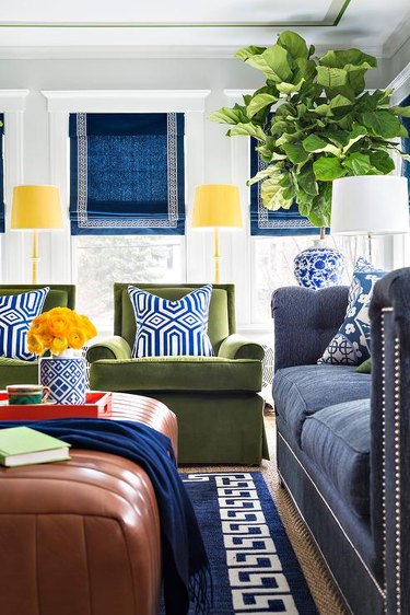 Living room with navy couch, rug, and shades, green chairs, and yellow lamps.