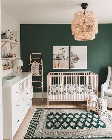 Gender neutral nursery with an emerald green paint, wicker light fixture and an oriental rug.