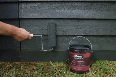 Rolling dark gray paint onto cedar shed