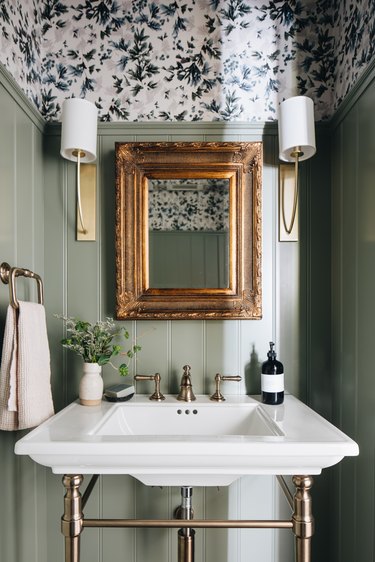 bathroom with white sink, mirror and two lamps, painted in light green with patterned upper area