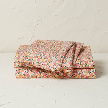 A folded pile of sheets featuring a pink, yellow, orange, and green floral pattern.
