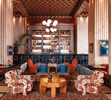 A mix of red-orange and blue printed textiles cover  all the seating in the large lounge area of the Peacock Bar