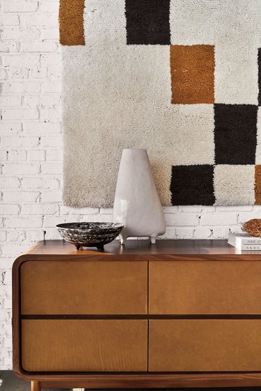 wood dresser in front of white brick wall with geometric wall hanging